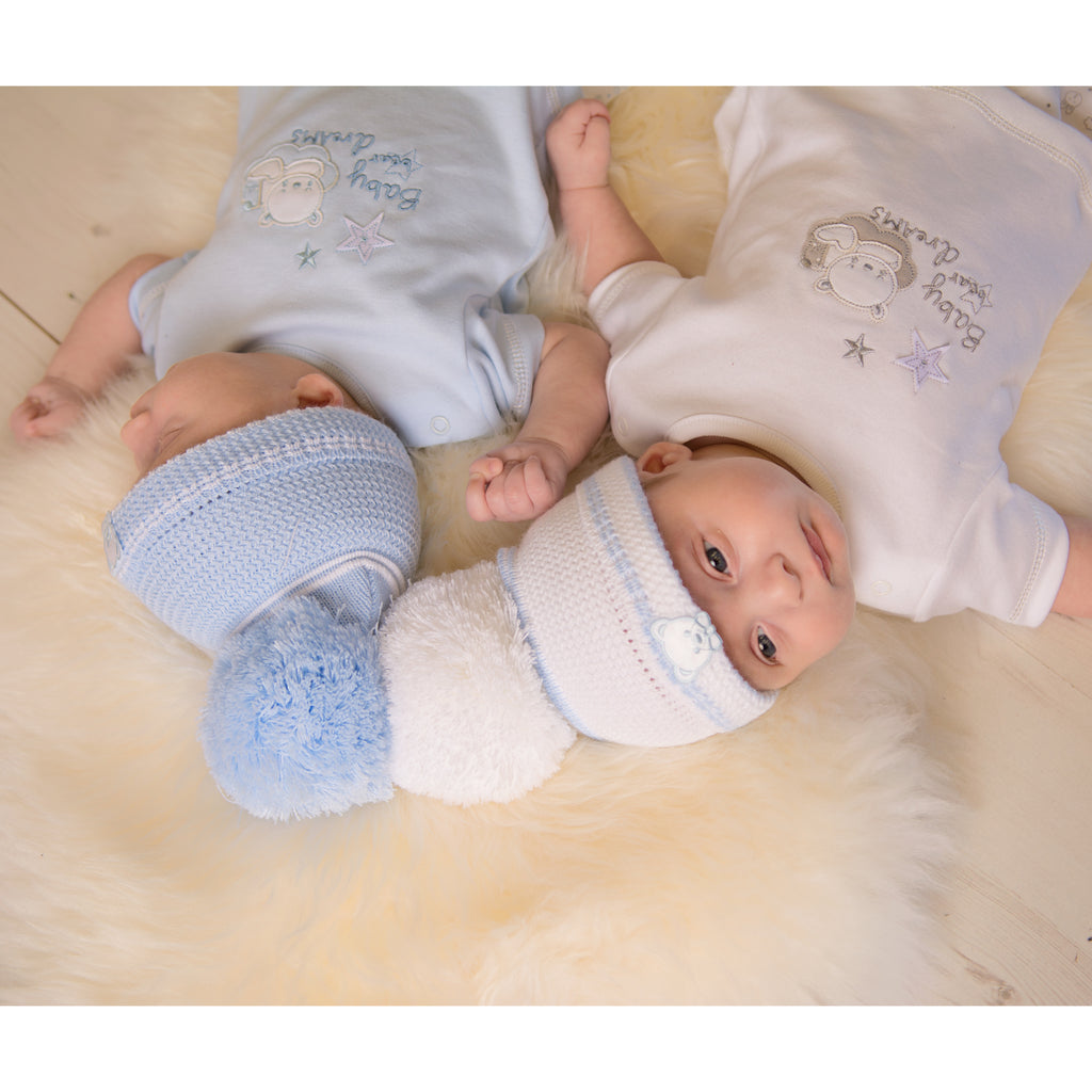 Two babies on a fur blanket, both wearing first size embroidered teddy hats